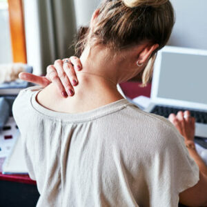 A person experiencing neck pain while sitting at a desk, likely related to poor posture or tension.
