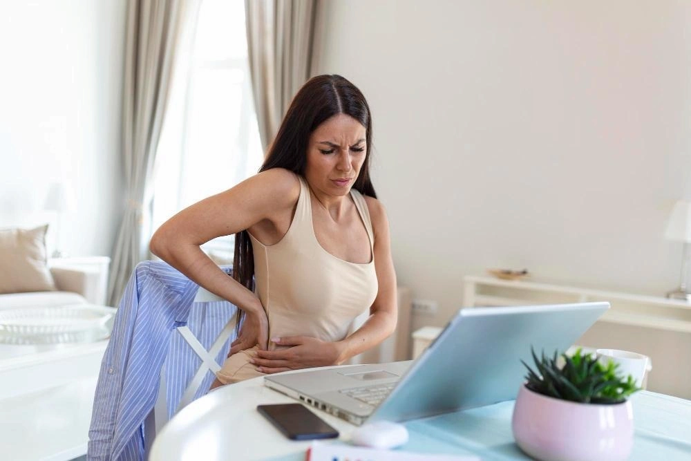 Businesswoman holding her back while working on laptop at home office