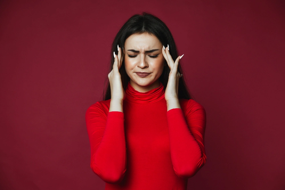 Woman holding head due to migraine or tension headache pain